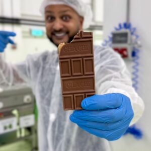 Cha Chi Versaci houdt een aangebroken chocoladereep omhoog met CHA CHI in de chocolade gedrukt.