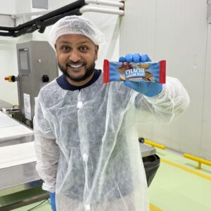 Cha Chi Versaci houdt een verpakte CHACHI Speculaas-reep van 70 gram omhoog in de fabriek.